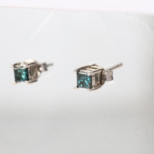 1129 - A pair of solitaire blue diamond earrings, claw set with Princess-cut diamonds with stud fittings, a... 