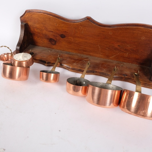 1006 - A graduated set of copper pans with brass handles, largest 10cm diameter, with an oak wall-mounted h... 