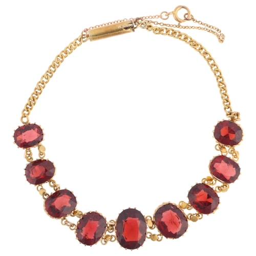 1161 - An Edwardian graduated garnet line bracelet, claw set with oval mixed-cut garnets, on curb link chai... 