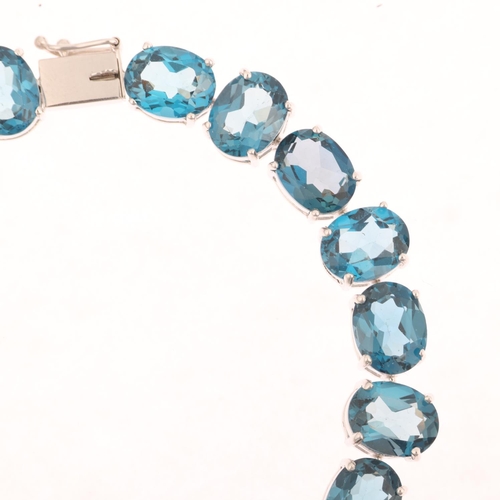 1306 - A modern 9ct white gold blue topaz tennis line bracelet, claw set with oval mixed-cut topaz, 20cm, 2... 