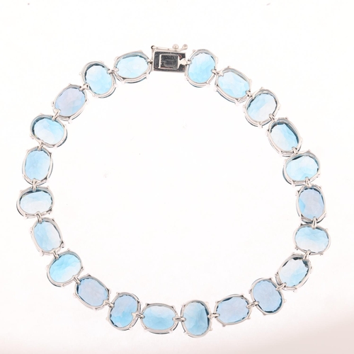 1306 - A modern 9ct white gold blue topaz tennis line bracelet, claw set with oval mixed-cut topaz, 20cm, 2... 