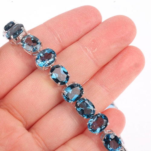 1306 - A modern 9ct white gold blue topaz tennis line bracelet, claw set with oval mixed-cut topaz, 20cm, 2... 