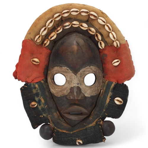 766 - A Dan hardwood Tribal mask in cowrie shell and textile surround, height 31cm