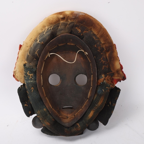 766 - A Dan hardwood Tribal mask in cowrie shell and textile surround, height 31cm