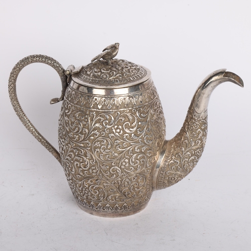 2765 - An Indian Kutch silver teapot, circa 1920, allover relief embossed floral decoration with bird knop,... 