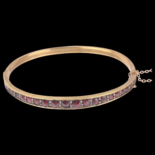 1400 - A Bohemian garnet hinged bangle, gilt-metal settings with graduated round faceted garnets, setting h... 