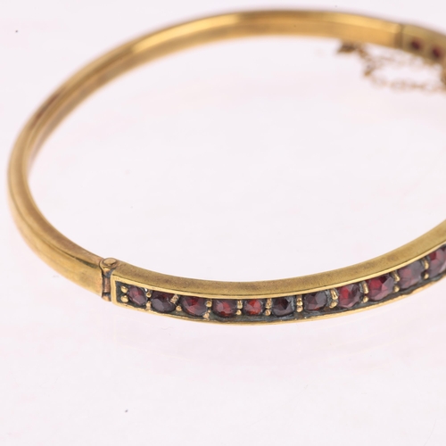 1400 - A Bohemian garnet hinged bangle, gilt-metal settings with graduated round faceted garnets, setting h... 