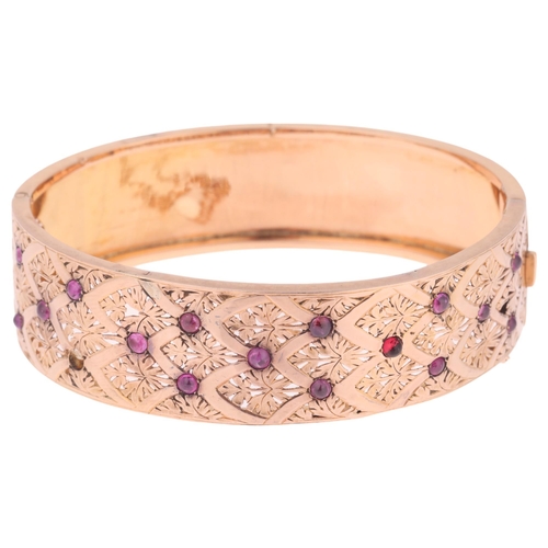 1129 - A French 18ct gold ruby hinged bangle, set with round cabochon rubies with pierced floral decoration... 