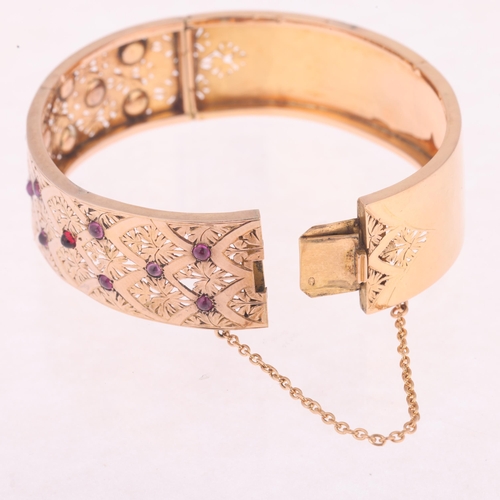 1129 - A French 18ct gold ruby hinged bangle, set with round cabochon rubies with pierced floral decoration... 