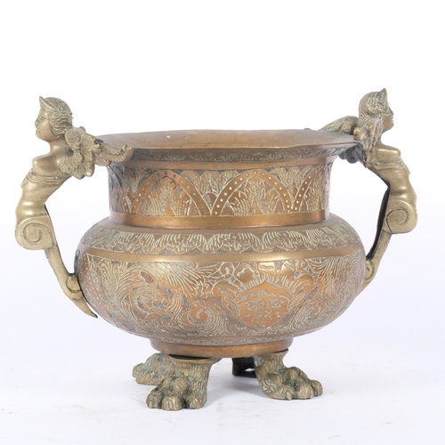 78 - A 19th century heavy engraved brass cauldron, with winged figure handles, raised on cast paw feet, H... 