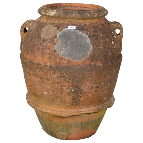 2802 - A large weathered terracotta olive oil jar, with two handles and armorial sunburst crest decoration.... 