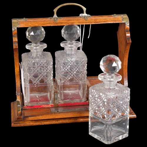 27 - A Gothic brass-mounted oak 3-bottle tantalus, with 3 hobnail glass square-section decanters and stop... 