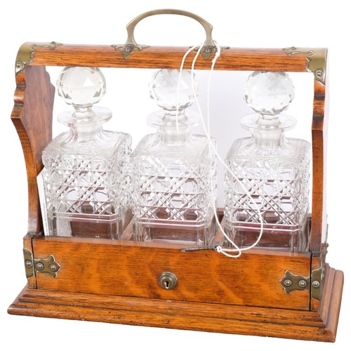 27 - A Gothic brass-mounted oak 3-bottle tantalus, with 3 hobnail glass square-section decanters and stop... 