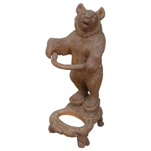 A late 19th century German Black Forest bear stick stand, modelled standing upright with original glass eyes, holding a branch form stick holder in its paws, on a naturalistic base (lacking insert), H87cm