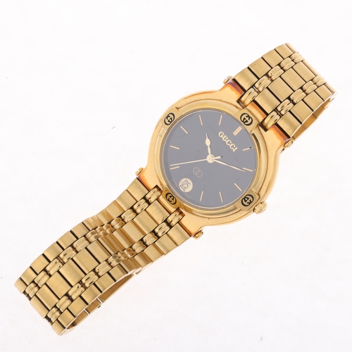 1048 - GUCCI - a gold plated 9200M quartz calendar bracelet watch, black dial with gilt baton hour markers,... 