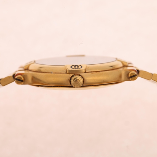 1048 - GUCCI - a gold plated 9200M quartz calendar bracelet watch, black dial with gilt baton hour markers,... 