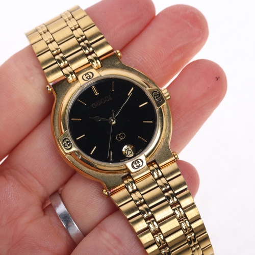 1048 - GUCCI - a gold plated 9200M quartz calendar bracelet watch, black dial with gilt baton hour markers,... 