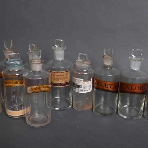 3020 - A group of 18 clear glass apothecary bottles, each with stopper, all have period labels of varying t... 