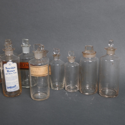 3020 - A group of 18 clear glass apothecary bottles, each with stopper, all have period labels of varying t... 