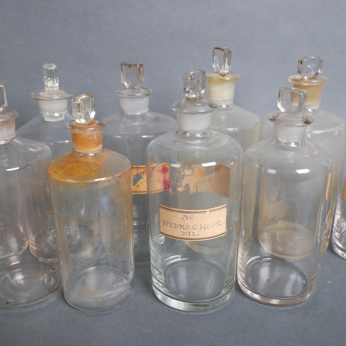 3030 - A group of 14 clear glass apothecary bottles, each with stopper, several have hand written period pa... 