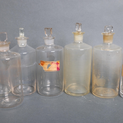 3030 - A group of 14 clear glass apothecary bottles, each with stopper, several have hand written period pa... 