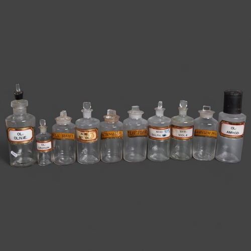 3032 - A group of ten clear glass apothecary bottles, each with stoppers, two with pouring tops, all have e... 