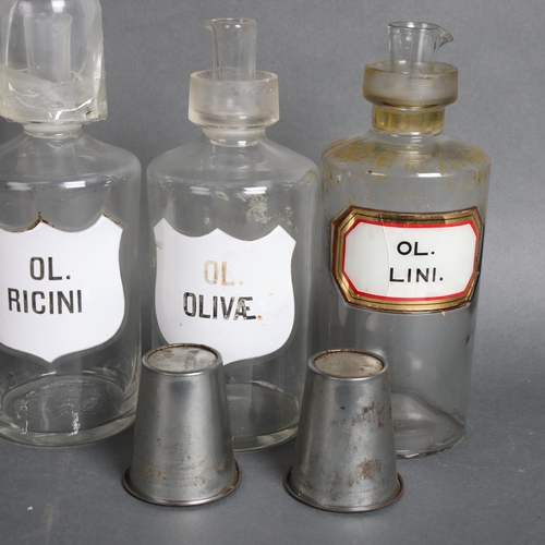 3040 - A group three clear glass apothecary bottles, each labelled, two with enamel labels, two with metal ... 