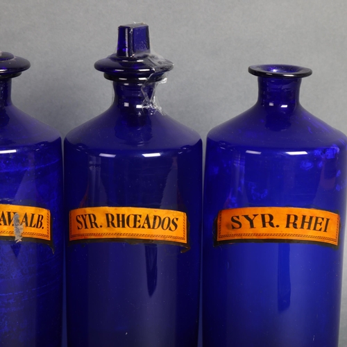 3045 - A group of four large blue glass apothecary bottles, three with stoppers, each with paper labels, la... 