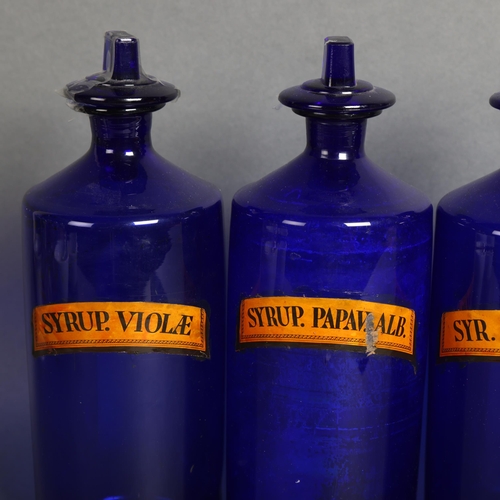 3045 - A group of four large blue glass apothecary bottles, three with stoppers, each with paper labels, la... 