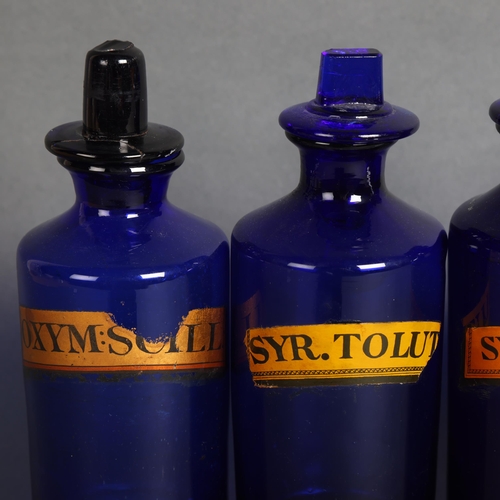 3047 - A group of four blue glass apothecary bottles with stoppers, each has paper label, largest height 22... 