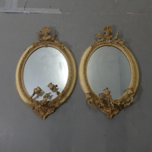 2710 - A pair of gilt-painted oval wall mirrors with sconces and pediments. Width 46cm, height 70cm.