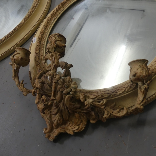 2710 - A pair of gilt-painted oval wall mirrors with sconces and pediments. Width 46cm, height 70cm.