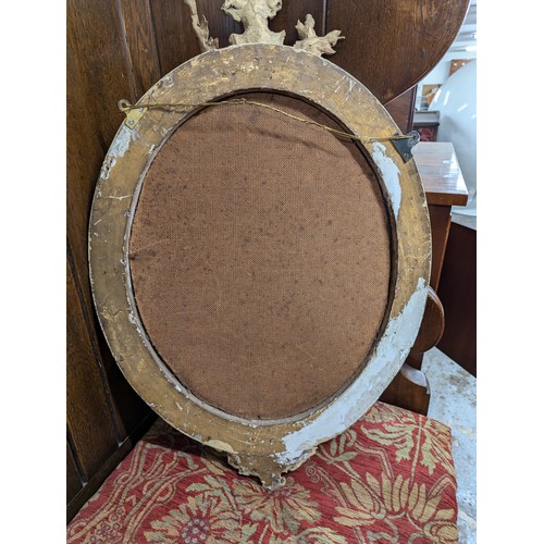 2710 - A pair of gilt-painted oval wall mirrors with sconces and pediments. Width 46cm, height 70cm.