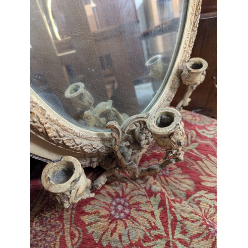 2710 - A pair of gilt-painted oval wall mirrors with sconces and pediments. Width 46cm, height 70cm.