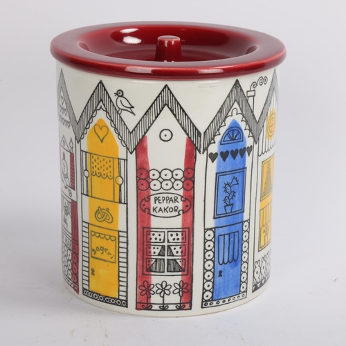 103 - A porcelain cylindrical Jar with red lid, decorated in multi colours with a terrace of rustic houses... 