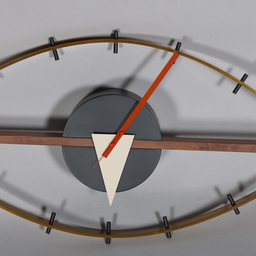 143 - A mid-century design wall clock in the form of an eye, the brushed brass frame curving around a waln... 