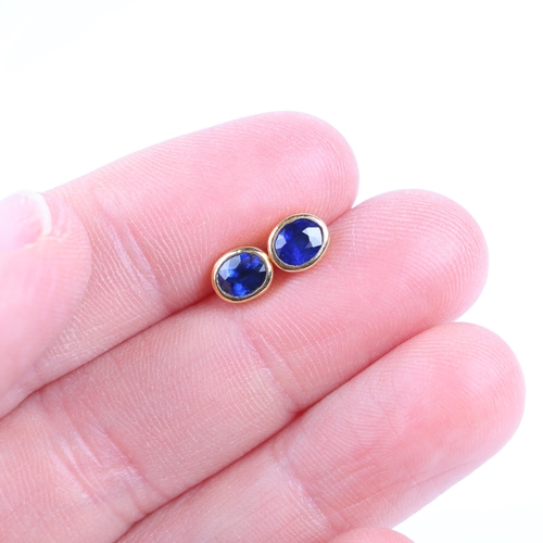 1256 - A pair of 22ct gold single stone sapphire stud earrings, each rub-over set with oval mixed-cut sapph... 