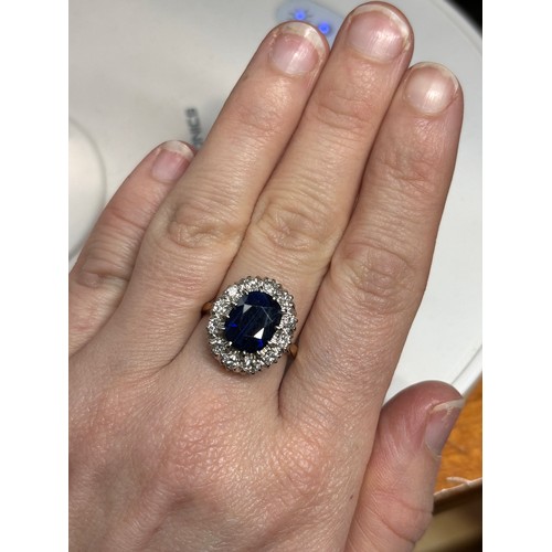 1145 - An 18ct gold sapphire and diamond cluster ring, claw set with 3.7ct oval mixed-cut sapphire surround... 