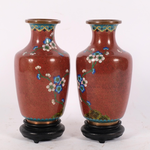 161 - A pair of Oriental red ground cloisonne vases, with coloured enamel prunus decoration, on turned woo... 