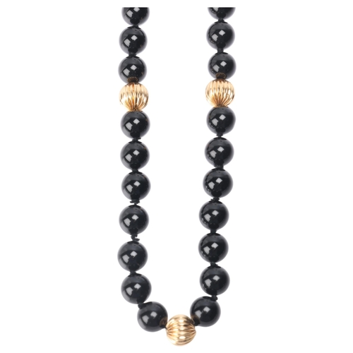 1138 - A long single strand 14ct gold onyx bead necklace, set with 10mm onyx beads having 7 x 14ct gold flu... 