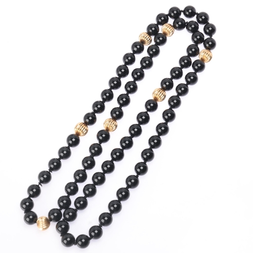 1138 - A long single strand 14ct gold onyx bead necklace, set with 10mm onyx beads having 7 x 14ct gold flu... 