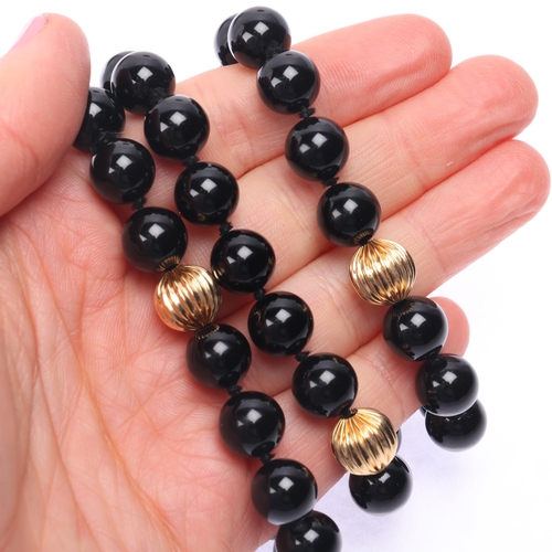 1138 - A long single strand 14ct gold onyx bead necklace, set with 10mm onyx beads having 7 x 14ct gold flu... 