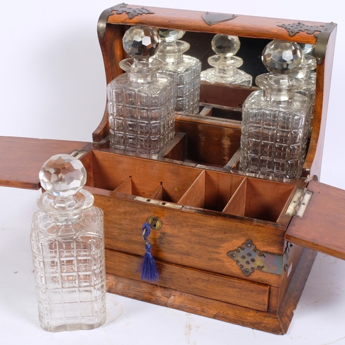 28 - An Edwardian brass-mounted oak 3-bottle tantalus, applied Gothic strapwork with mirror-back decanter... 