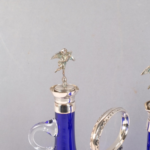 70 - A pair of hand-blown blue glass oil/vinegar bottles, with plated cherub stoppers on plated stand, H2... 