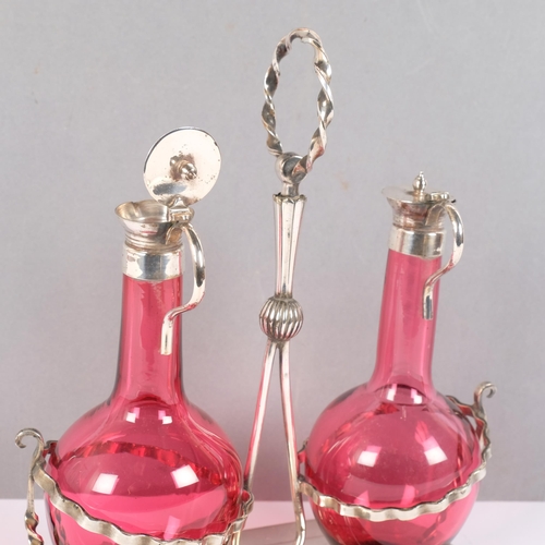 71 - A pair of hand-blown cranberry glass oil/vinegar bottles, with hinged plated tops, on a plated stand... 