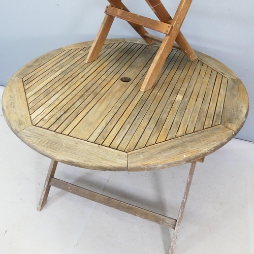 2487 - A weathered teak folding circular top garden table. Diameter 112cm, height 75cm, and similar chair.