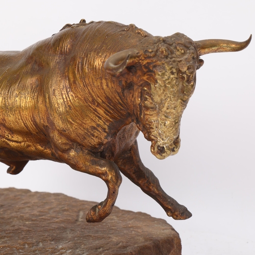 312 - A gilt-bronze charging bull, late 19th/early 20th century, unsigned on natural stone base, overall l... 