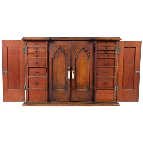 A 19th century oak table-top collector's cabinet, Ecclesiastical design, in inverted break-front form, having 4 lancet-top panelled doors, completely fitted with 24 short drawers, 62cm x 44cm x 29cm