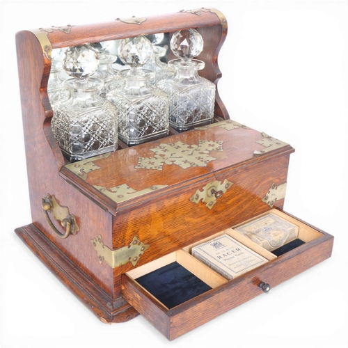 61 - A Victorian oak tantalus with 3 square cut-glass decanters, fold-out lids enclosing 3 liqueur glasse... 