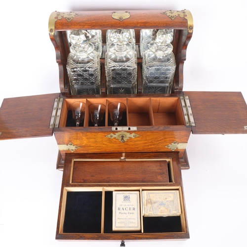 61 - A Victorian oak tantalus with 3 square cut-glass decanters, fold-out lids enclosing 3 liqueur glasse... 